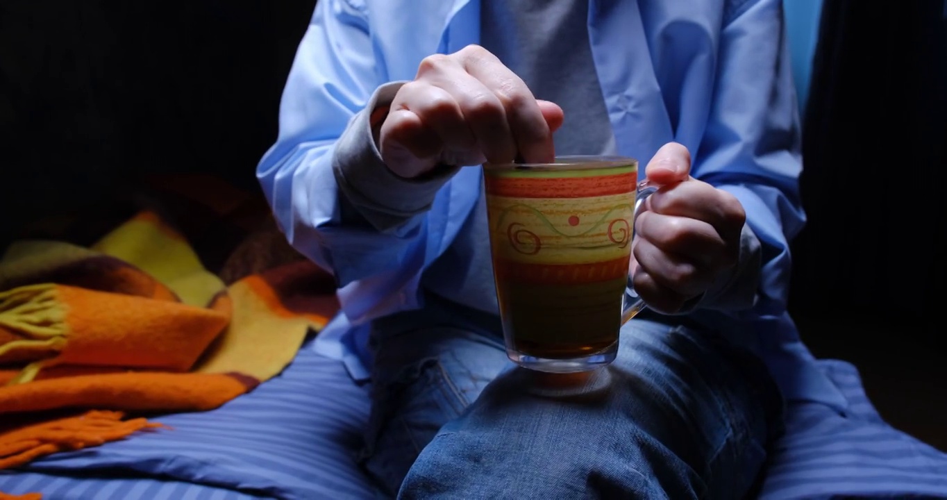 一个不认识的人正坐在沙发上搅动茶杯里的茶视频下载