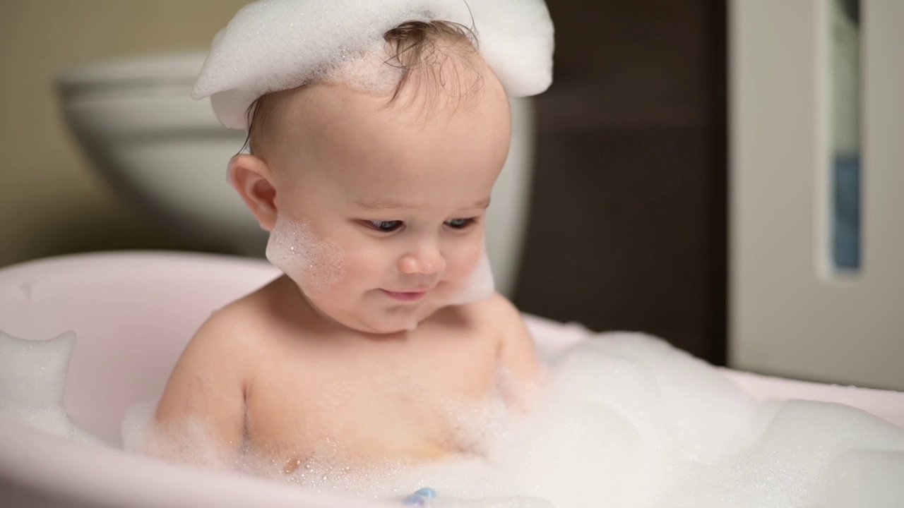 一个小男孩坐在泡着泡沫的浴缸里，可爱地抬头看着，转头视频素材