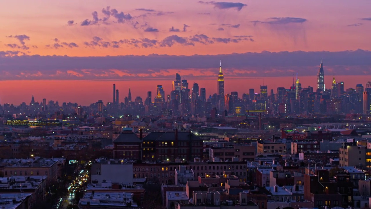 远处的曼哈顿天际线在日落时分照亮了布鲁克林布什维克住宅区的夜空。无人机视频与平移摄像机运动。视频素材