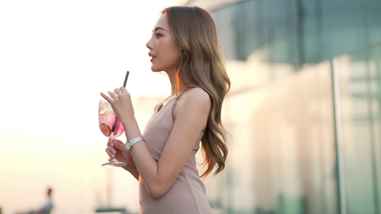 日落时分，一名4K亚洲女子在摩天大楼的屋顶餐厅喝着鸡尾酒等朋友。视频下载