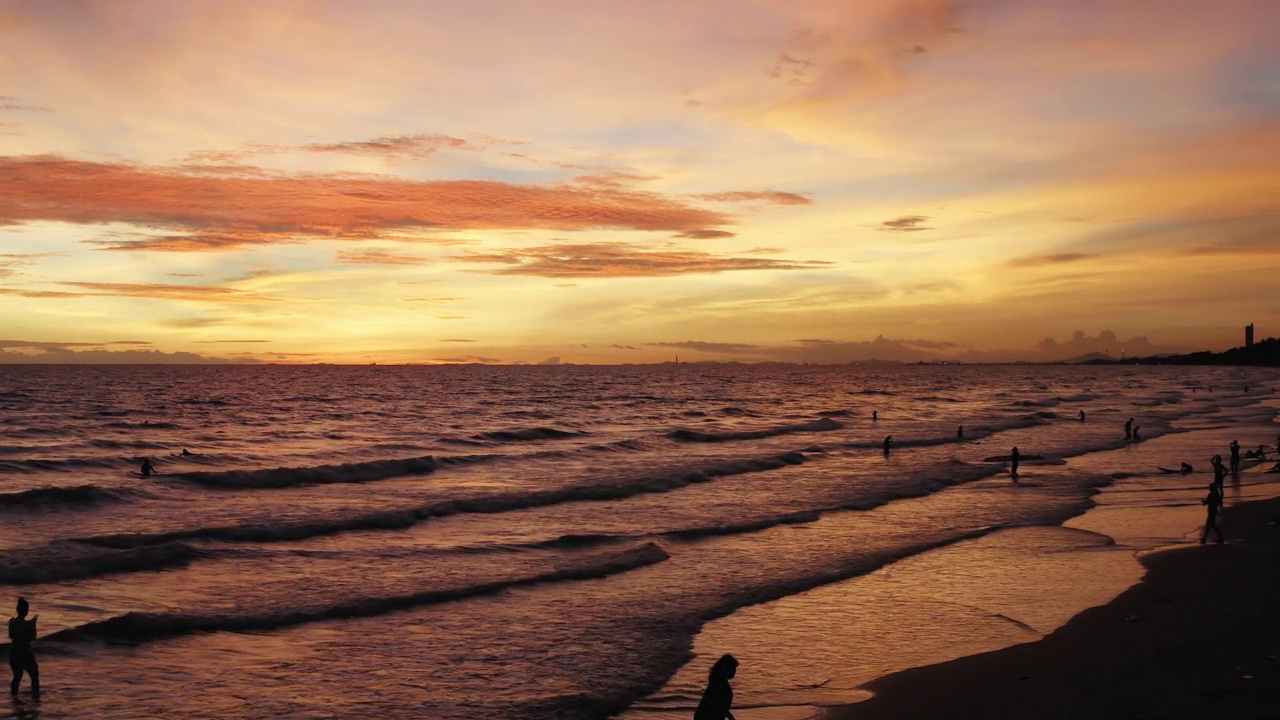 在淡季，秋天的日落时分，游客在海滩上冲浪的无人机鸟瞰图。放松的健康生活方式。视频下载