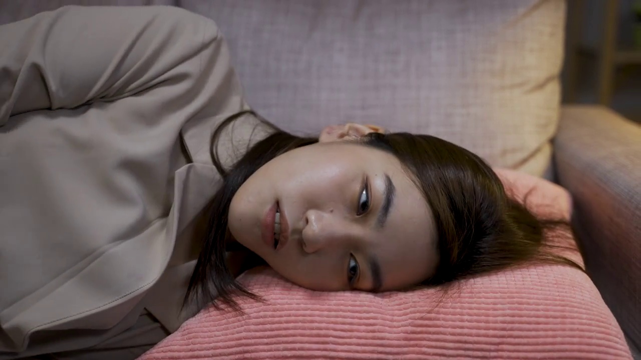慢镜头:疲惫的亚洲女企业家在下班回家后，一头扎进沙发的枕头上，用手梳理着疲惫的头发。视频素材