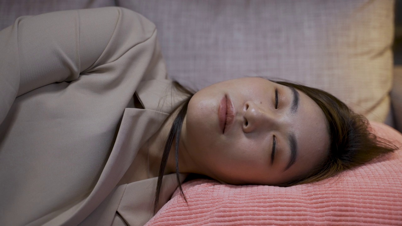头部特写慢镜头，一名亚洲女经理在家里辛苦工作后倒在客厅的沙发上，凝视着枕头上的空间。视频素材