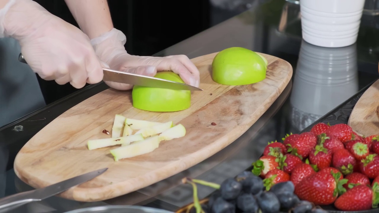 一个年轻的女人在厨房的木板上切着一个新鲜的青苹果。健康食品的概念视频下载