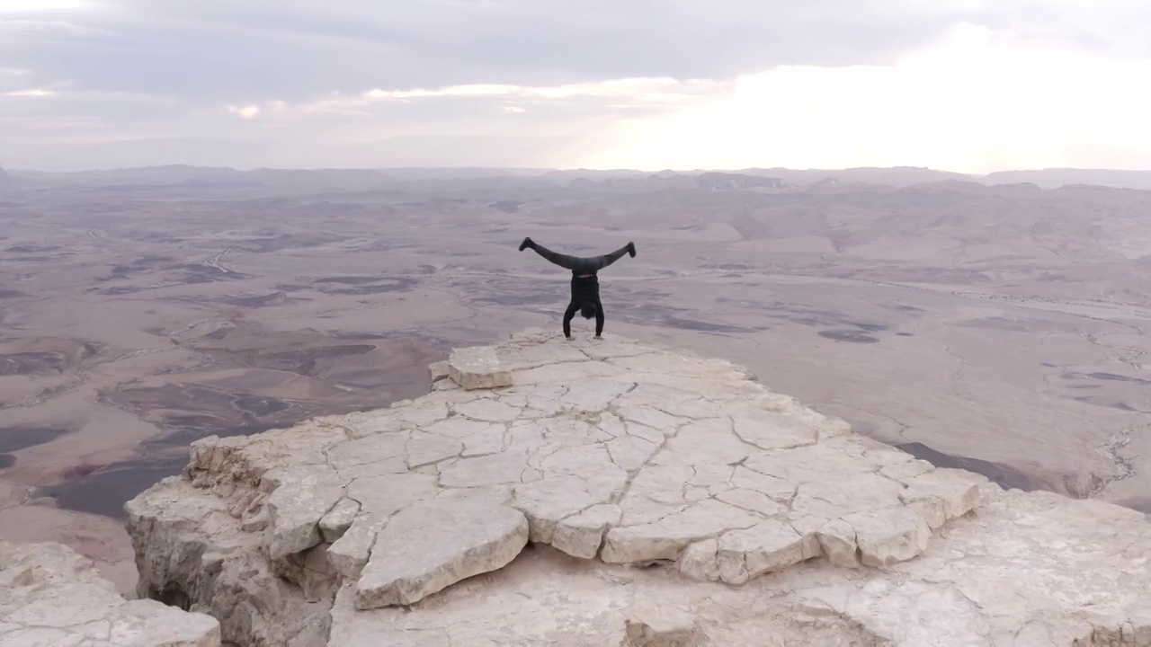 男子倒立在沙漠悬崖边缘，鸟瞰图视频素材