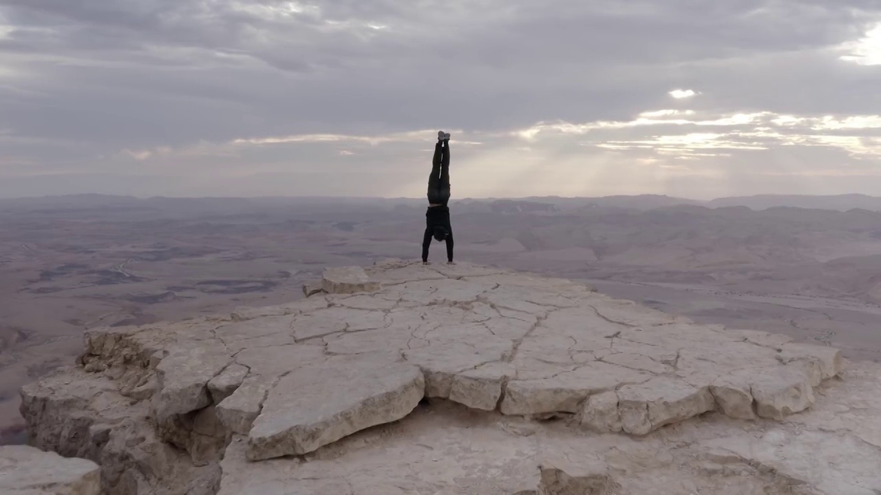 男子倒立在沙漠悬崖边缘，鸟瞰图视频素材
