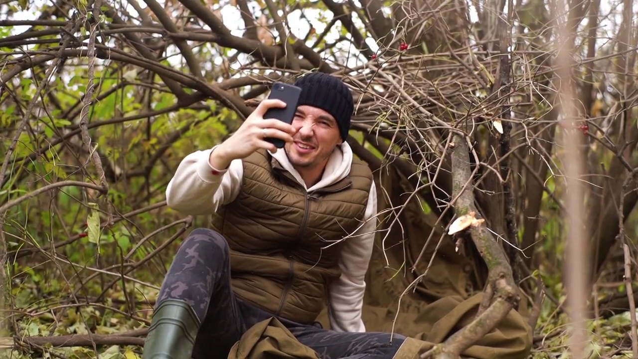 迷路的旅行者男性穿着暖和的衣服，坐在森林里，试图在阴冷的天气捕捉手机信号。视频素材