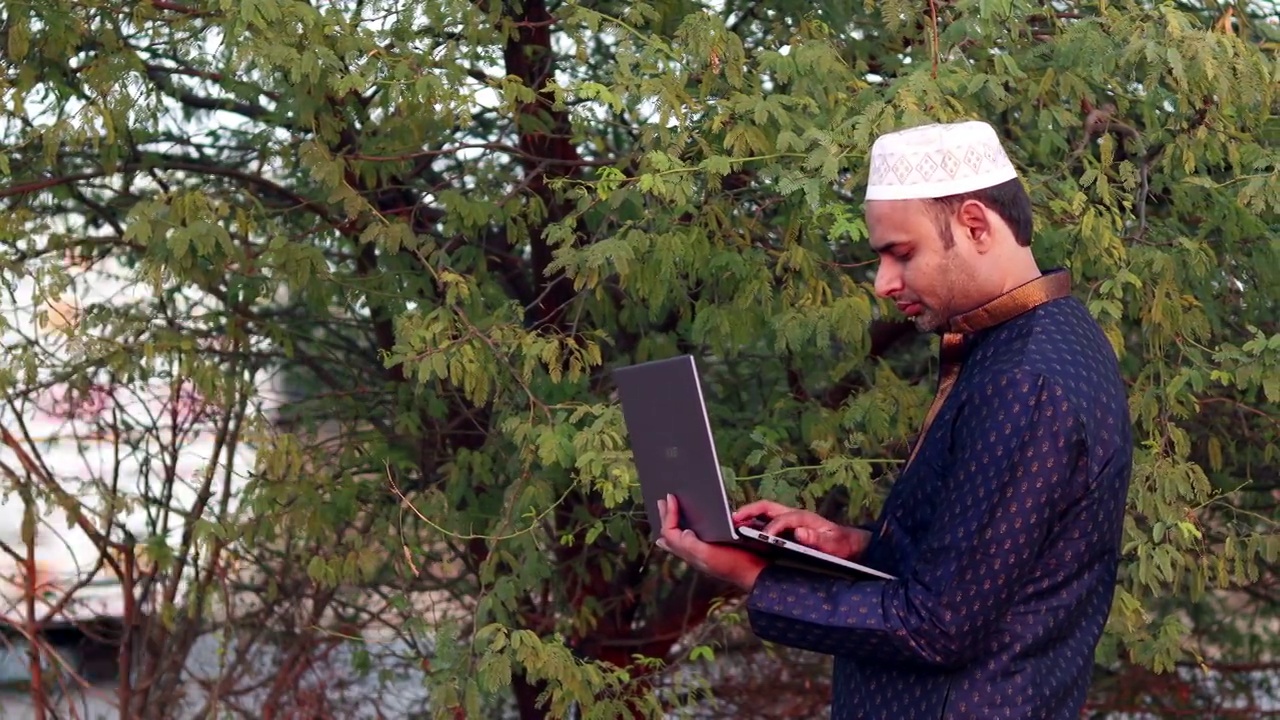 年轻的印度穆斯林男子在自然背景下使用笔记本电脑视频素材