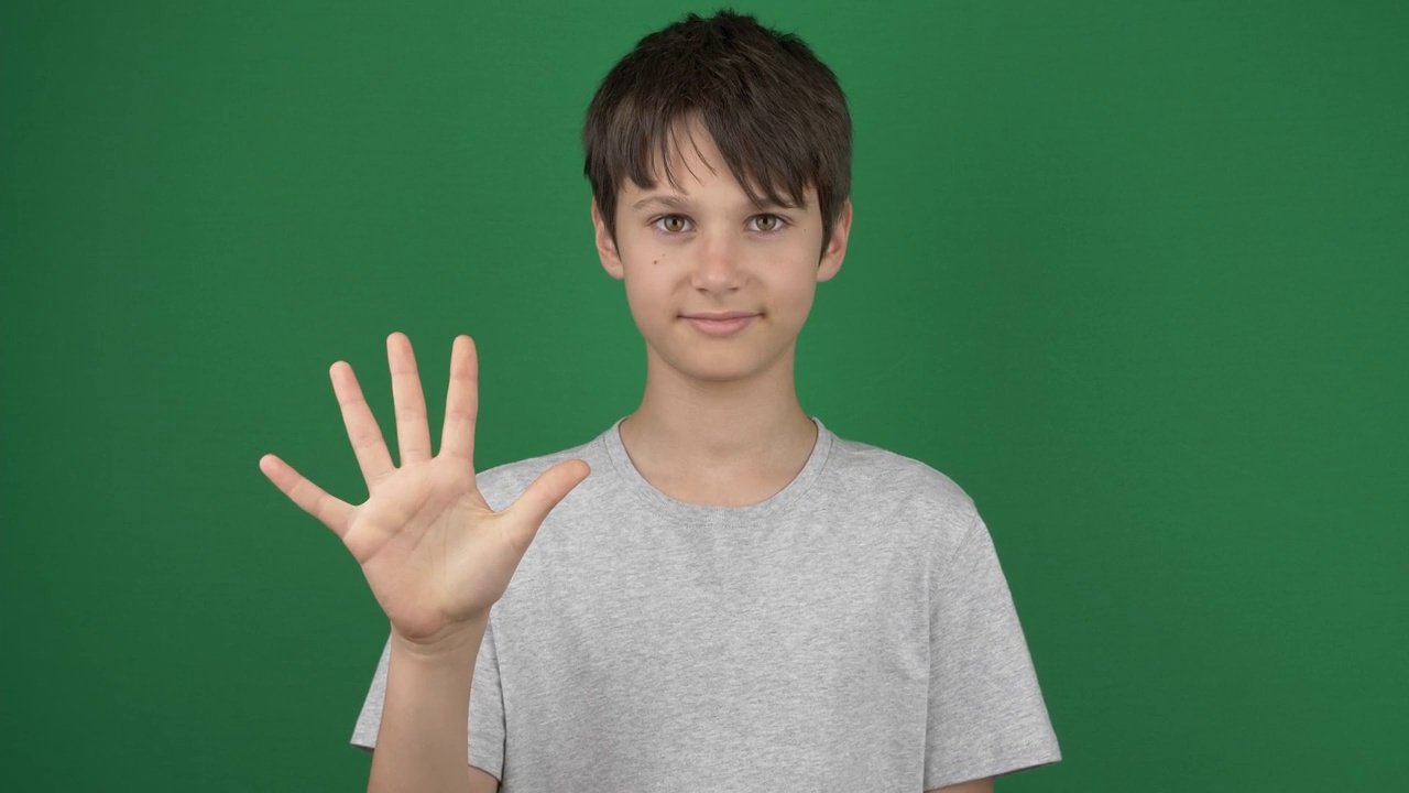 一个十几岁的男孩用手指从1到5显示数字，在绿色屏幕的色度键背景上数一、二、三、四、五视频素材