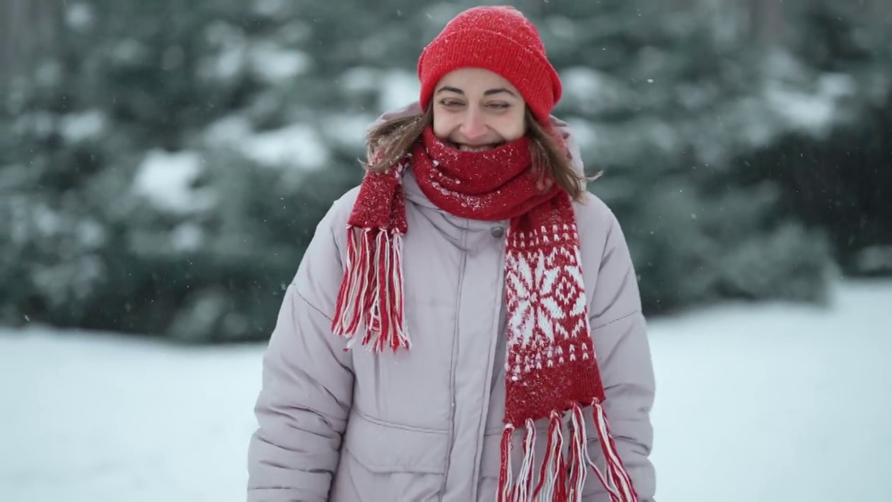 4k慢镜头跟踪拍摄下雪天，戴着红色手套和帽子的快乐漂亮女人在冷杉林中散步，在寒假里与雪嬉戏视频下载