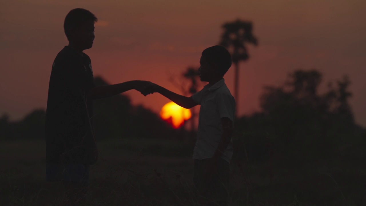 两个男孩在握手，夕阳的剪影视频素材