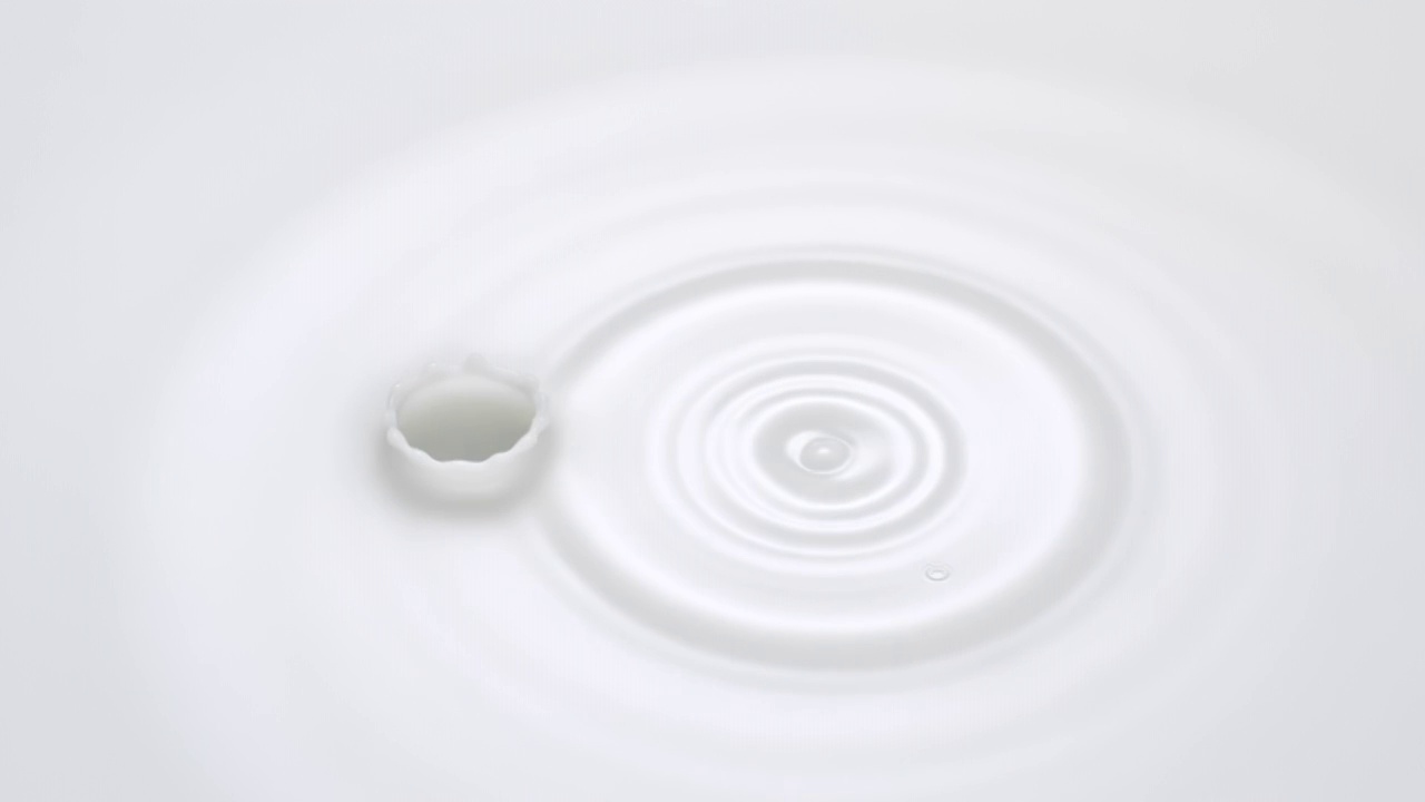 特写镜头和超慢动作与头顶的视图牛奶滴不断下降到一个白色的液体池，使涟漪和皇冠视频素材