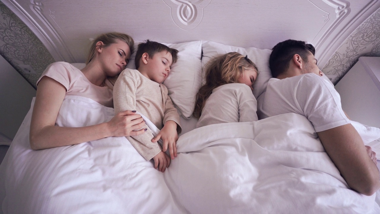 年轻轻松的家人，父母和孩子，睡在大床上视频下载