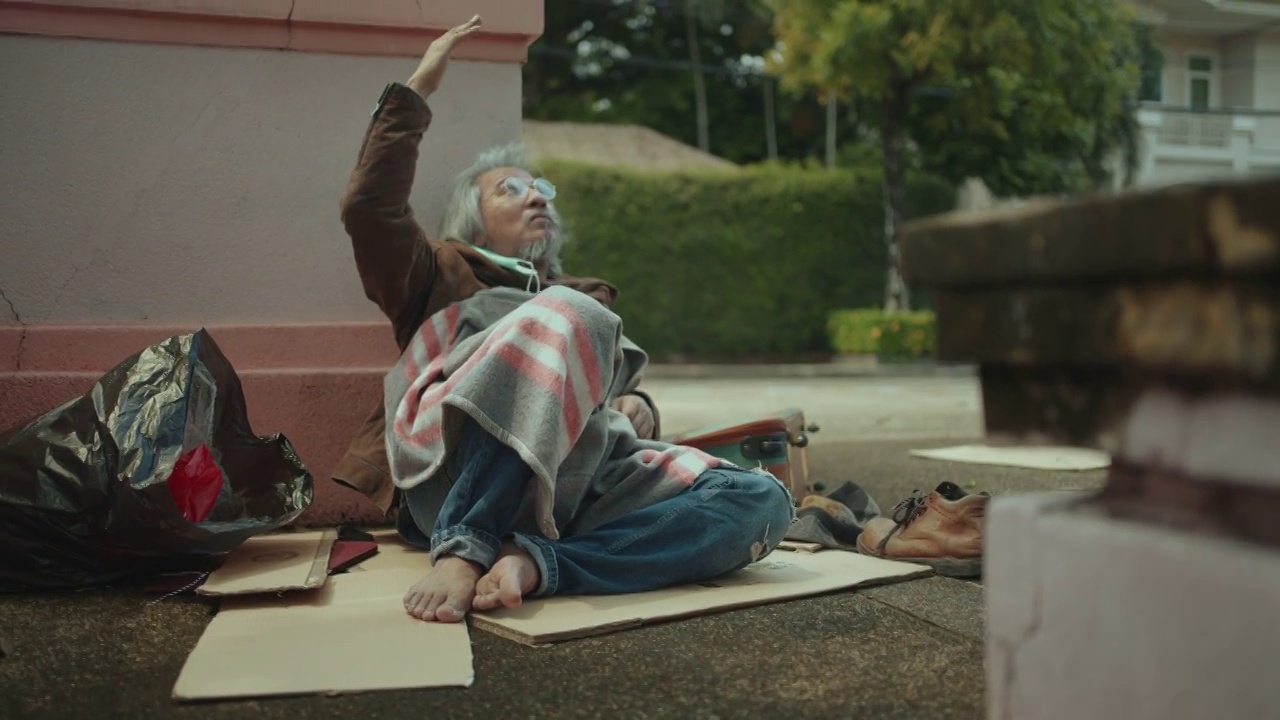 一个亚洲乞丐拿着他的包躺在人行道上，因为他在冠状病毒大流行期间失业了。视频下载
