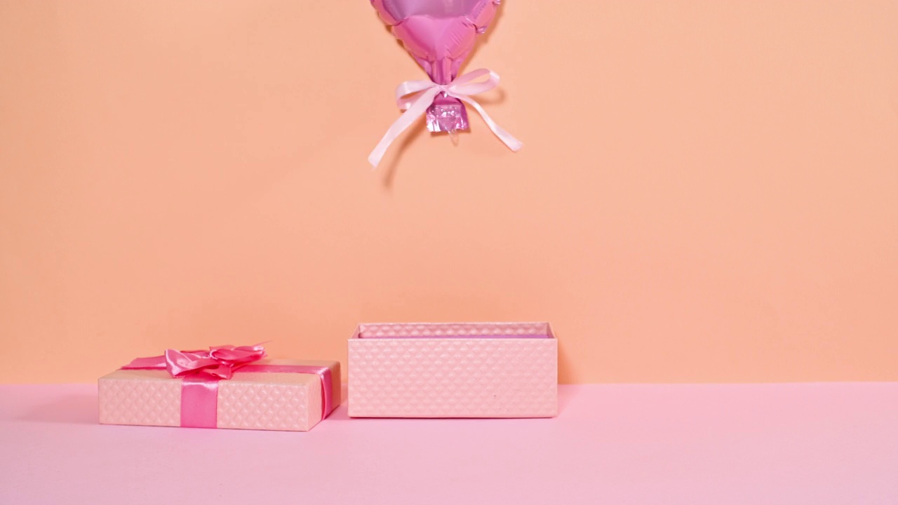 带丝带的粉色礼盒出现并打开，爱心气球从礼物中飞出。停止运动视频下载