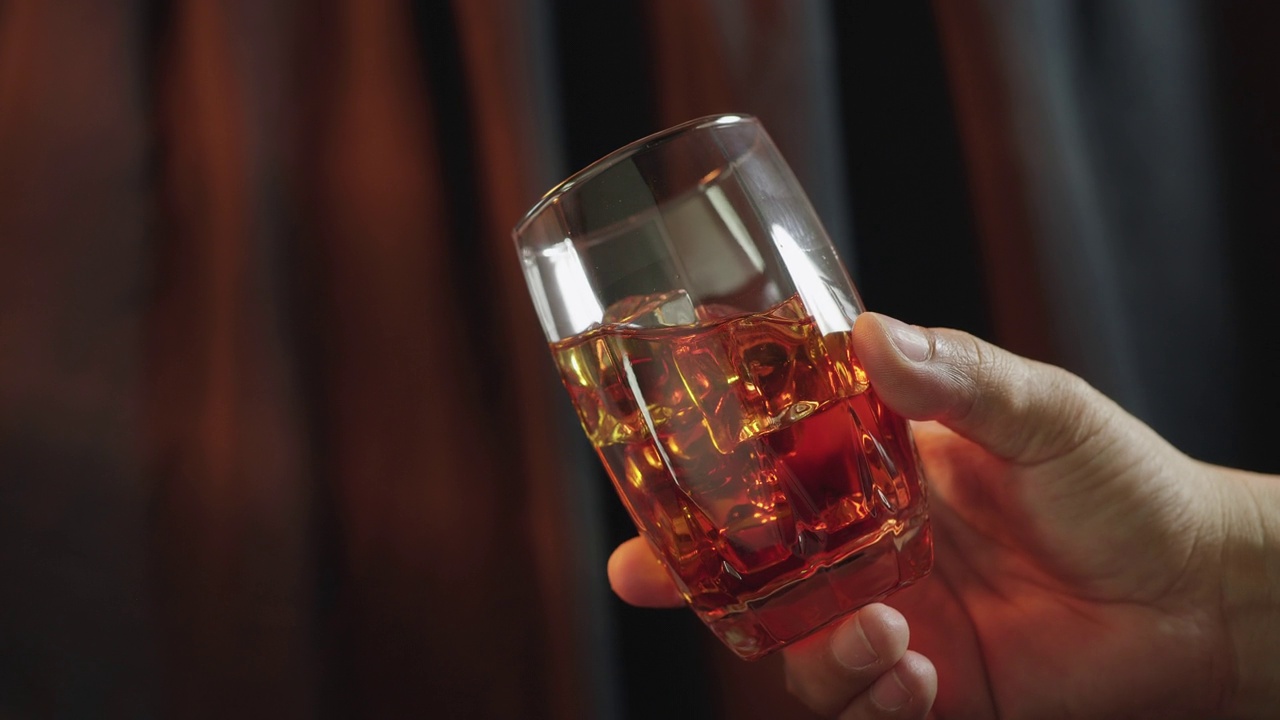 男人慢慢地在杯子里加入冰块搅拌金色威士忌视频素材