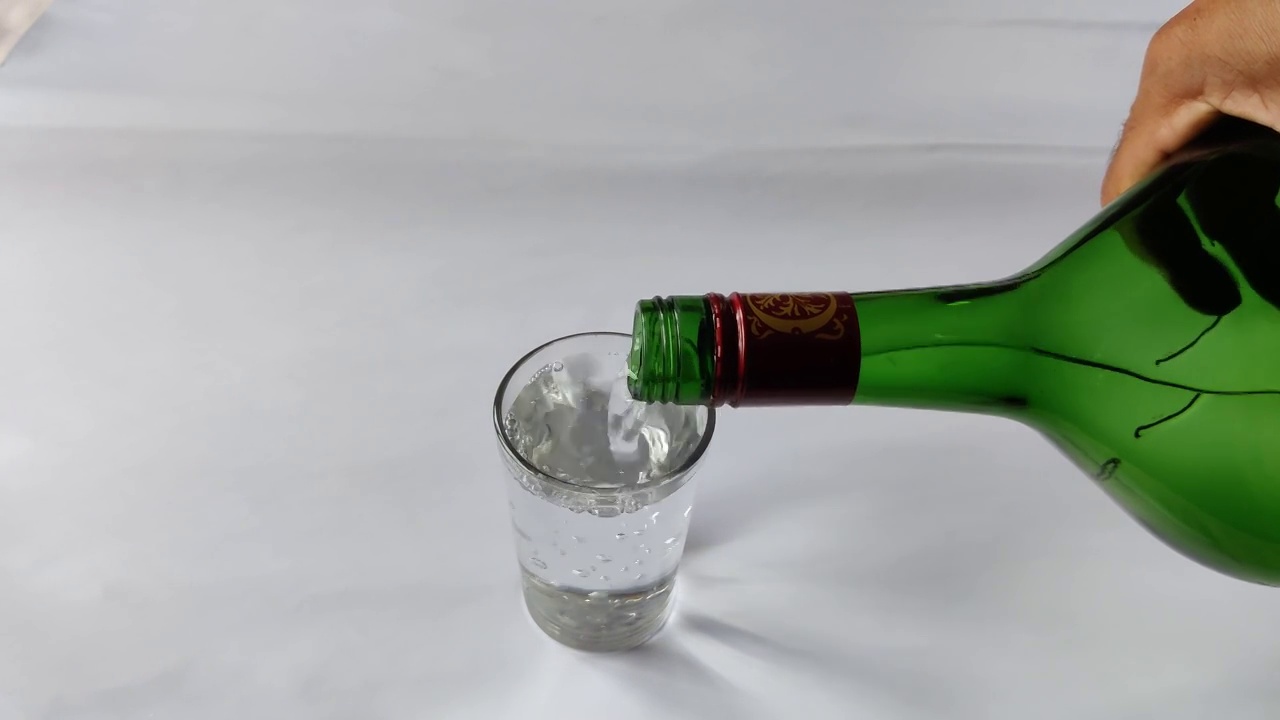 从绿色的玻璃瓶中倒水到水杯的特写镜头是白色的背景视频素材