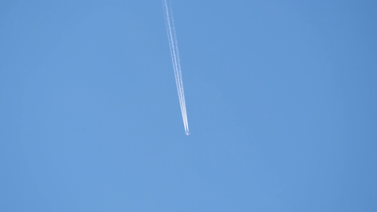 远处的喷气式客机在晴朗的蓝天上高空飞行，留下白色的烟迹。航空运输的概念视频素材