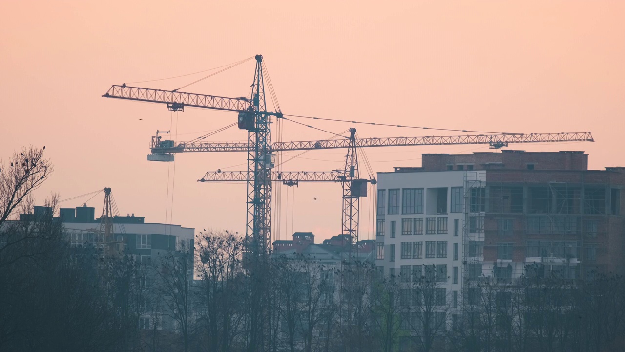 日落时分，在高层住宅楼施工现场，塔式起重机的黑色剪影。房地产开发。视频素材