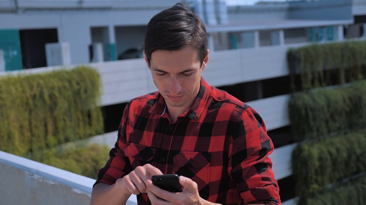 迷人的男子在格子衬衫使用智能手机触摸屏户外城市背景。设备、人、现代青年概念视频素材