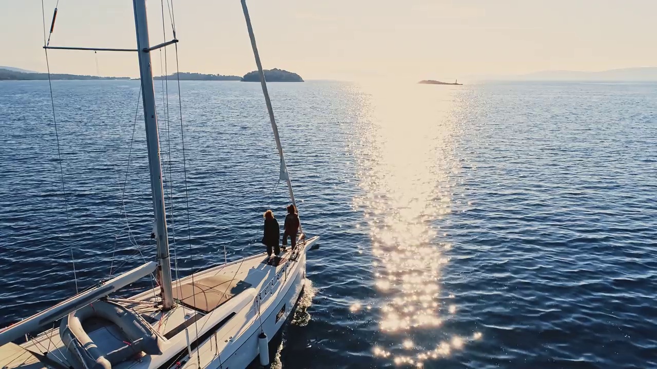 航拍日落时分，两名年轻女子站在帆船的甲板上享受微风视频下载