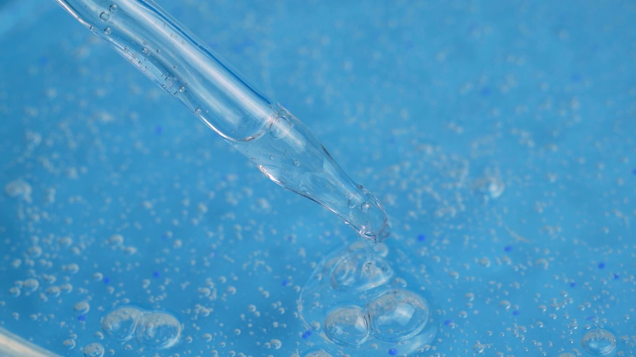 一股带着小气泡的透明化妆品凝胶滴落在蓝色的表面。精华液、抗衰老霜、洗发露、抗菌凝胶、透明质酸视频素材