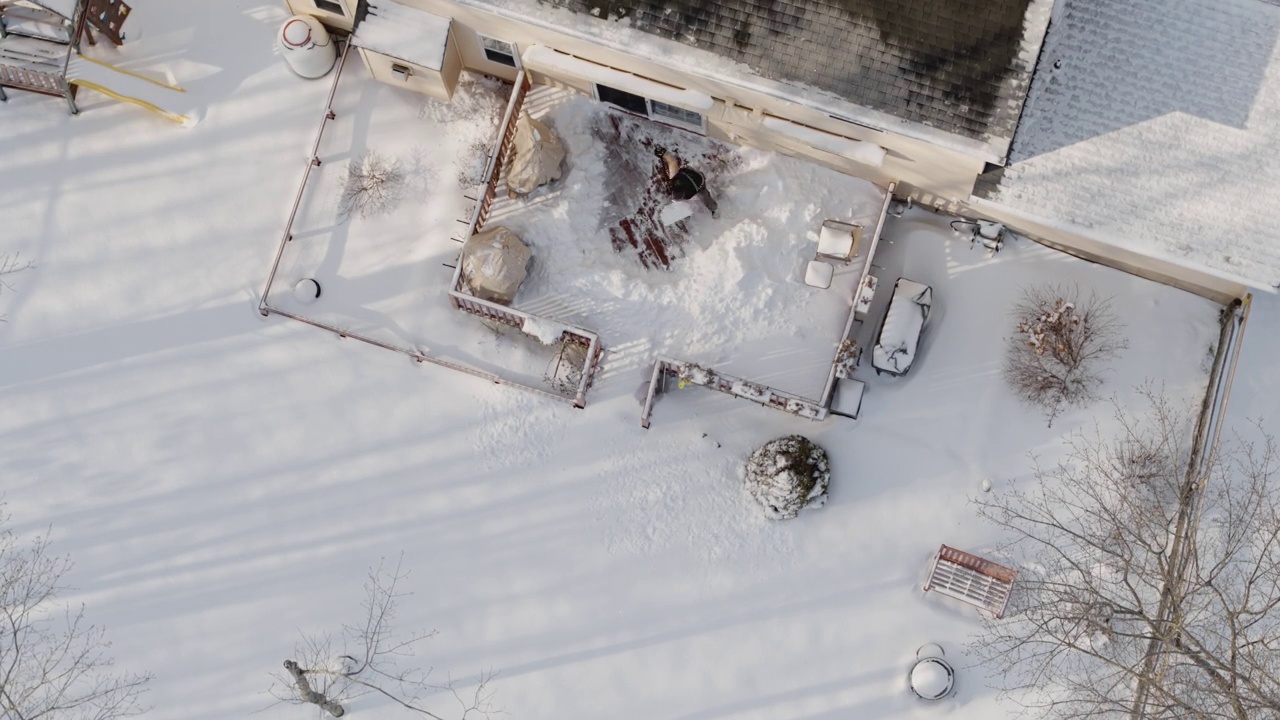 一个成年人在冬天下雪后用铲子清理门廊上的积雪。鸟瞰直接上方无人机加速，时间推移式视频。视频下载