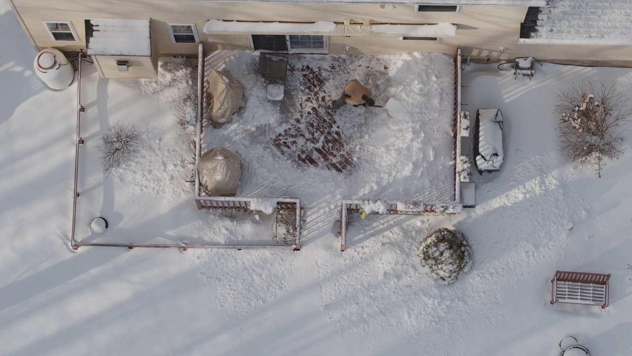 一个成年人在冬天下雪后用铲子清理门廊上的积雪。鸟瞰图直接在无人机视频上方。视频下载