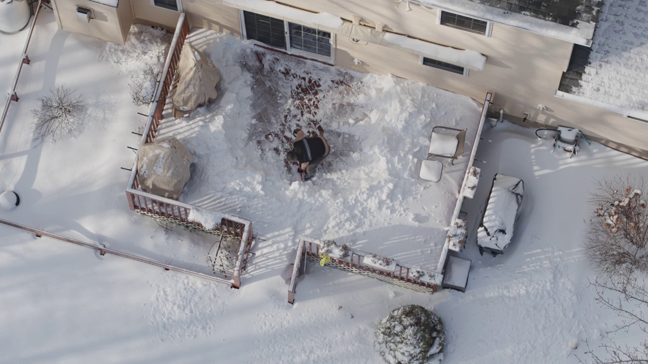 一个成年人在冬天下雪后用铲子清理门廊上的积雪。鸟瞰图直接上方的无人机慢动作视频。视频下载