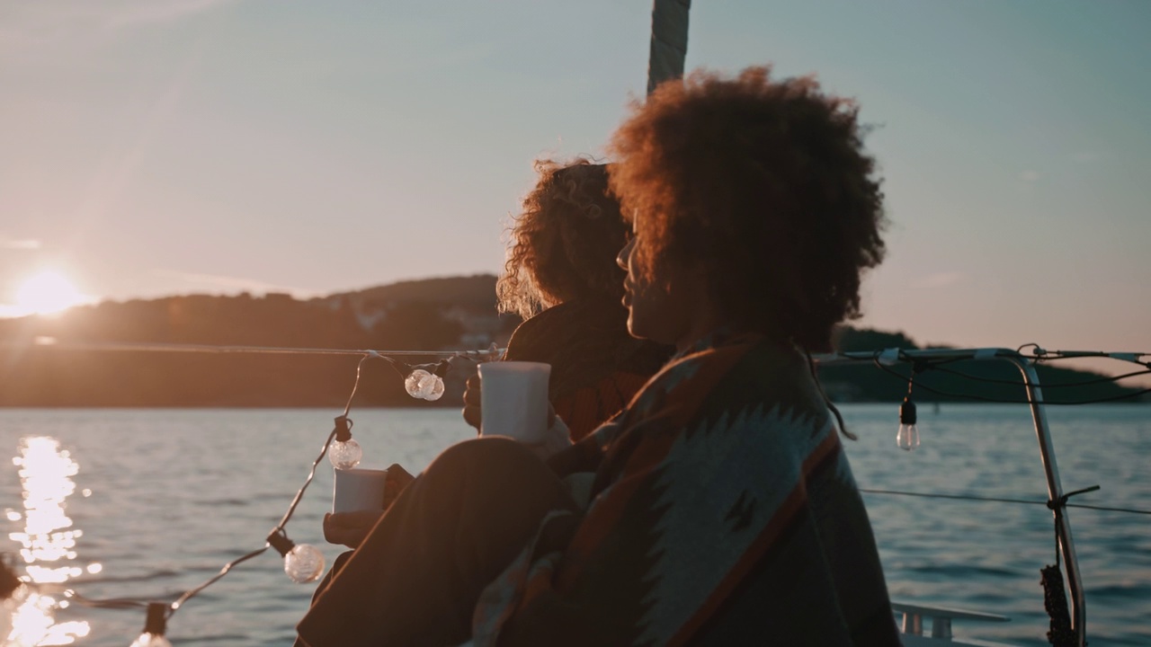 黄昏时分，两个年轻女子在帆船的甲板上喝热饮料视频下载