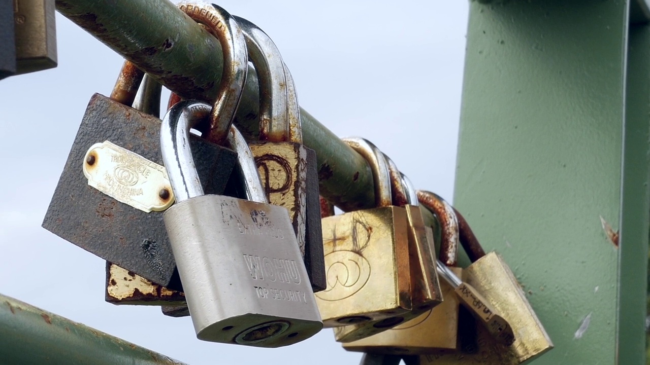 手拉手的女人在桥的铁栏杆上研究着与爱情相连的金属挂锁视频下载