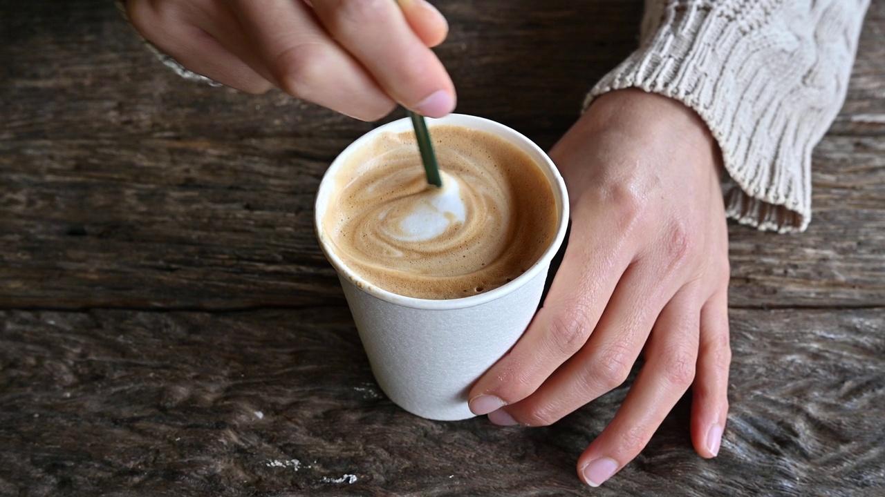 桌面视图的人使用勺子搅拌热拿铁咖啡在纸杯之前饮用。视频下载