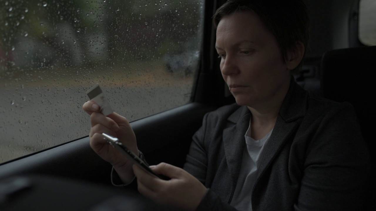 女商人在雨中坐在汽车后座使用信用卡和智能手机进行电子银行视频下载