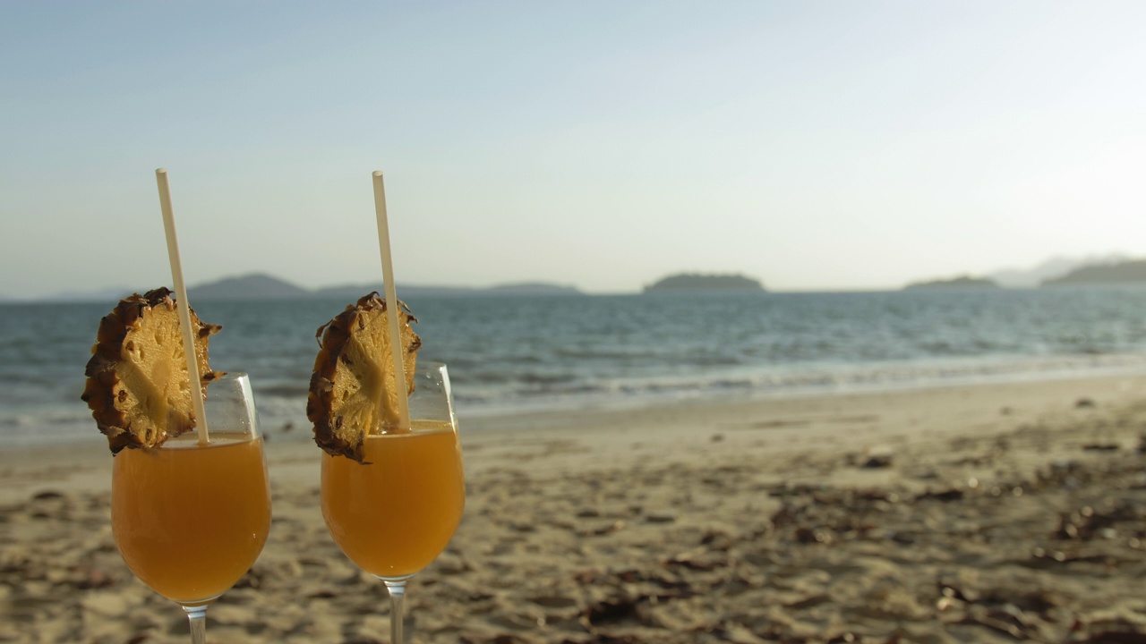 鸡尾酒椰林飘香，凤梨片，日落时分。模糊的背景海滩和大海。概念热带食品和饮料，酒精饮料视频素材