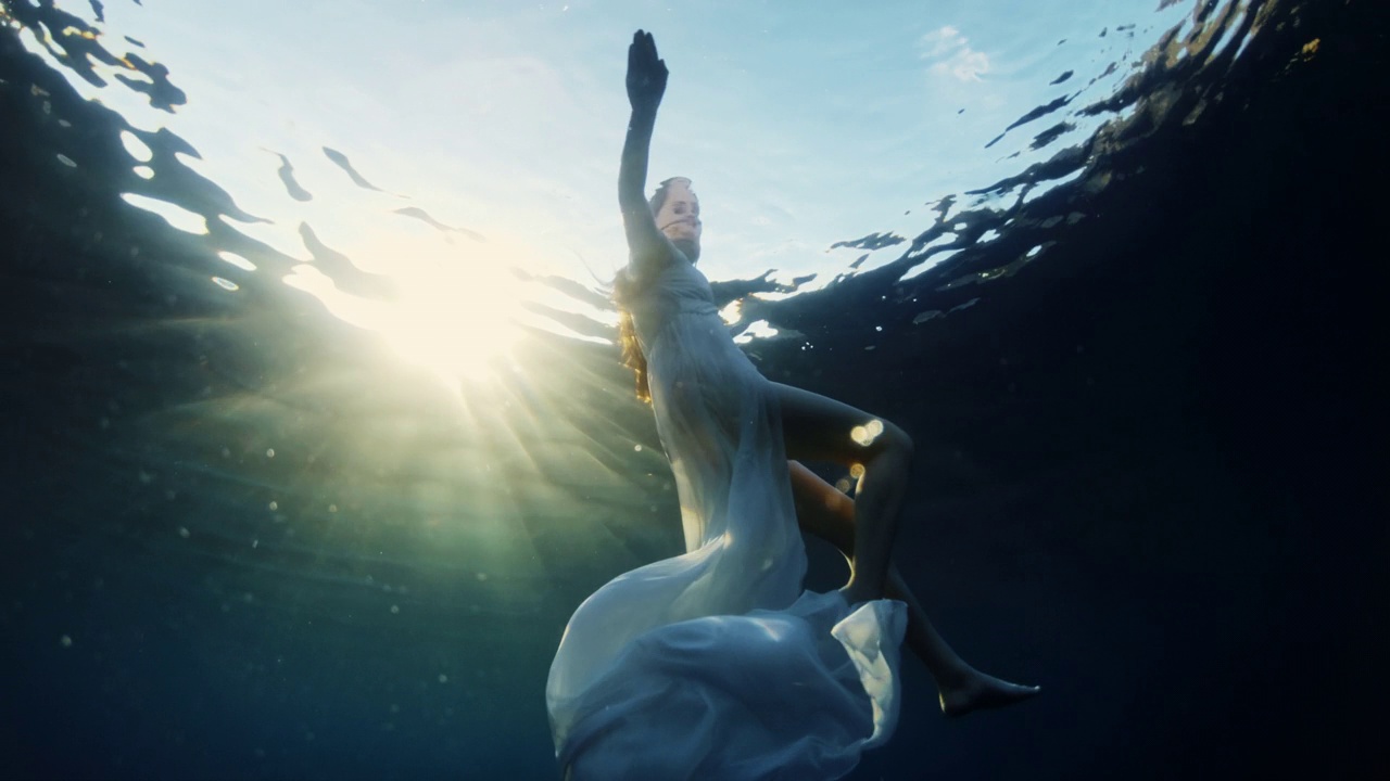 日落时，一名身穿白色连衣裙的年轻女子在海里游泳视频素材