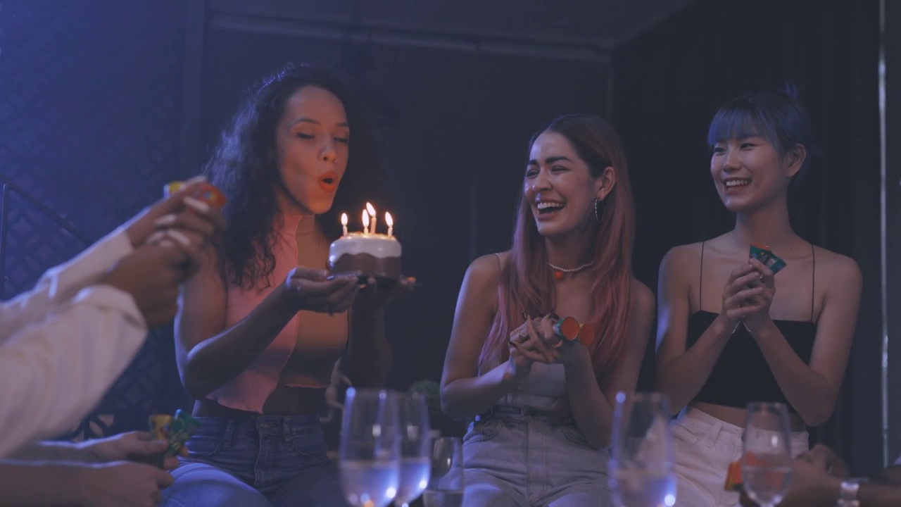各式各样的年轻人和时尚人士在晚上开派对，吹生日蛋糕上的蜡烛，同时放上五彩纸屑烟花视频下载