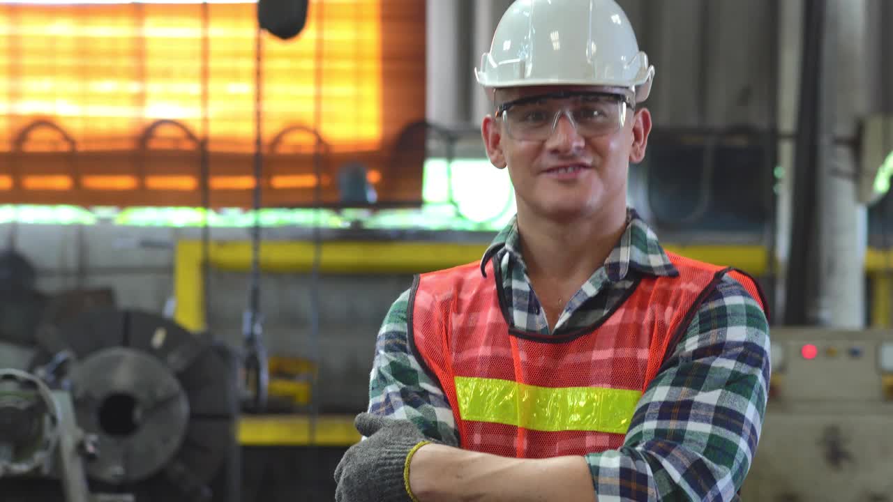 在工业工厂，自信的工头双手交叉，竖起大拇指，对着镜头微笑。建筑工地的蓝领工人视频素材