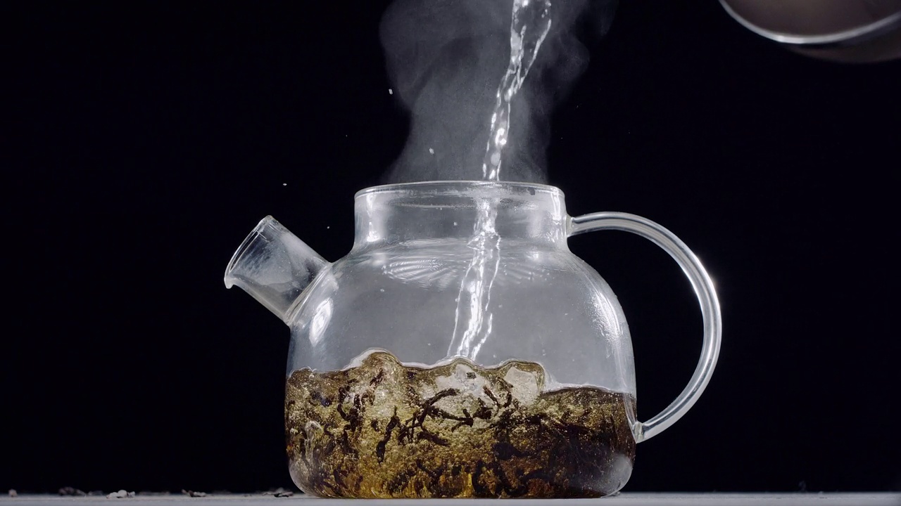 开水倒进一个大叶茶的玻璃茶壶，深棕色的背景，慢动作150帧每秒，Blackmagic Ursa Pro G2。视频下载