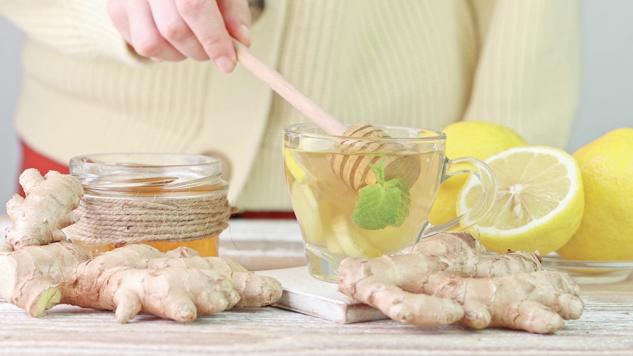 女手将蜂蜜和蜂蜜勺从罐子里取出放入盛有姜、柠檬和薄荷的茶杯中视频素材