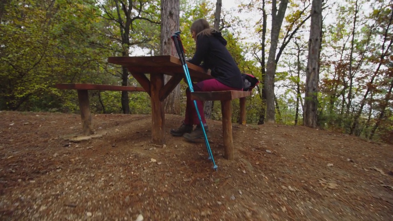 徒步旅行的女孩在山区森林的泥土路或小道上的木制长凳休息区自拍。秋天的户外旅行和健康的生活方式。视频下载