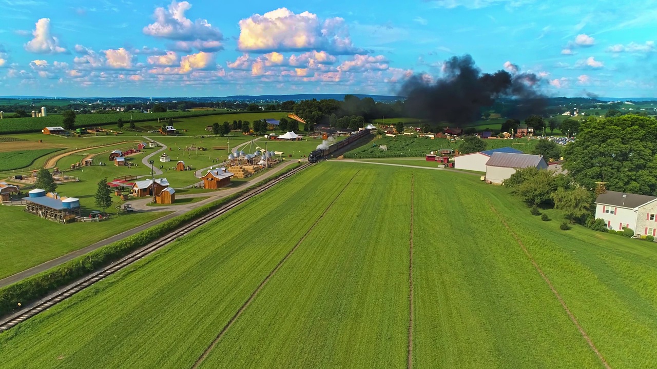 鸟瞰图，阿米什人的农场与一条铁路轨道和蒸汽客运火车接近视频素材
