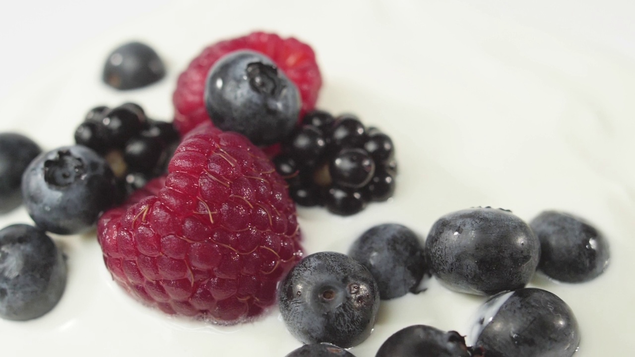 新鲜健康的食物。蓝莓和覆盆子、黑莓一起掉进酸奶里。鲜果淋上鲜奶油。有机浆果，清洁饮食，素食理念。慢动作视频素材