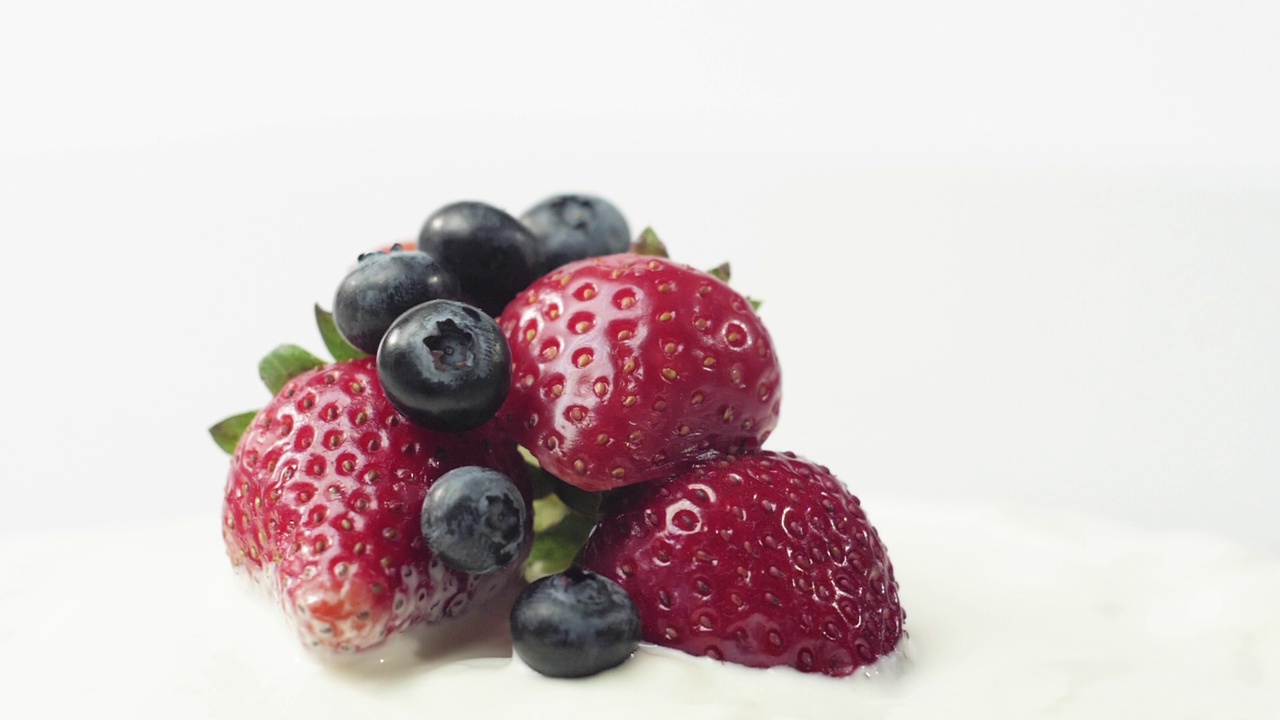 新鲜健康的食物。在酸奶和鲜奶油中放入草莓和蓝莓。鲜果配鲜奶油。有机浆果，清洁饮食，素食理念。慢动作视频素材