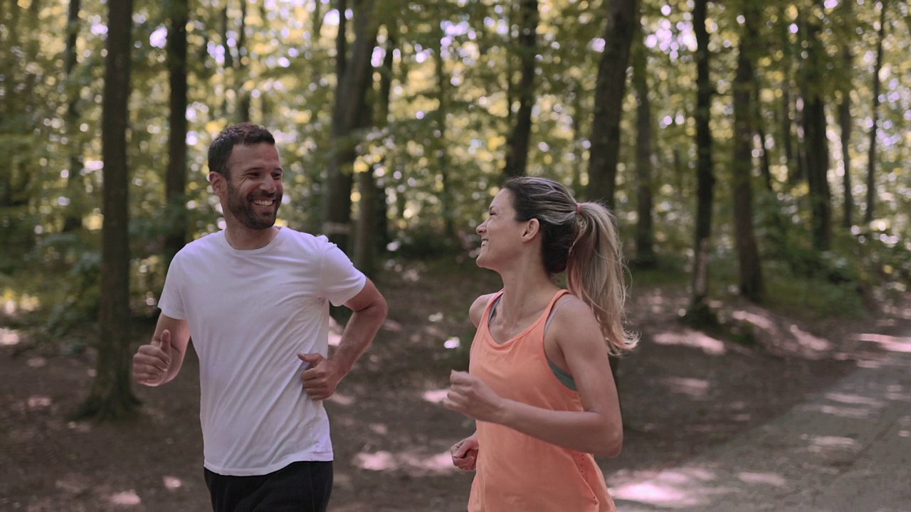 快乐的运动情侣一边在大自然中跑步一边聊天。视频下载