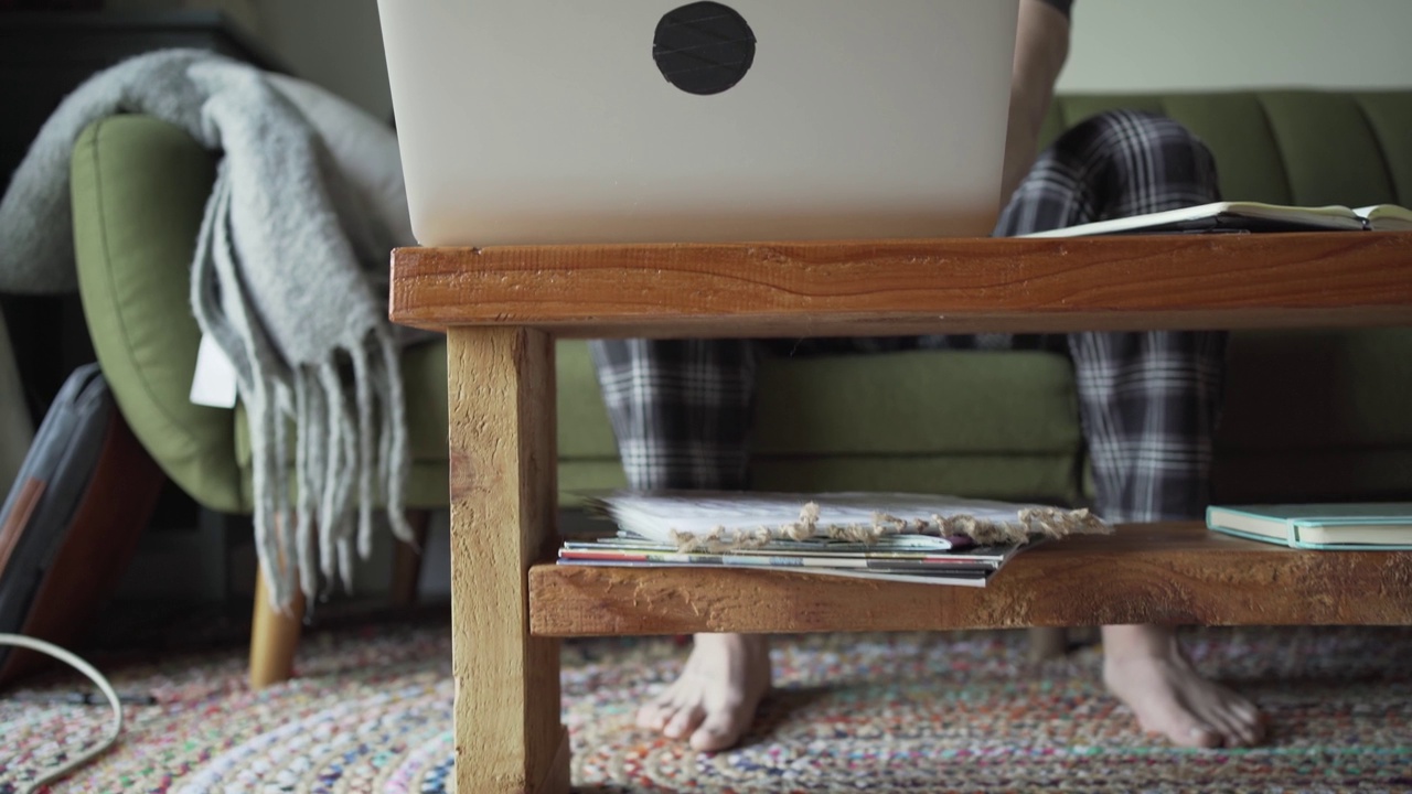 一个年轻人早上坐在沙发上用笔记本电脑视频素材