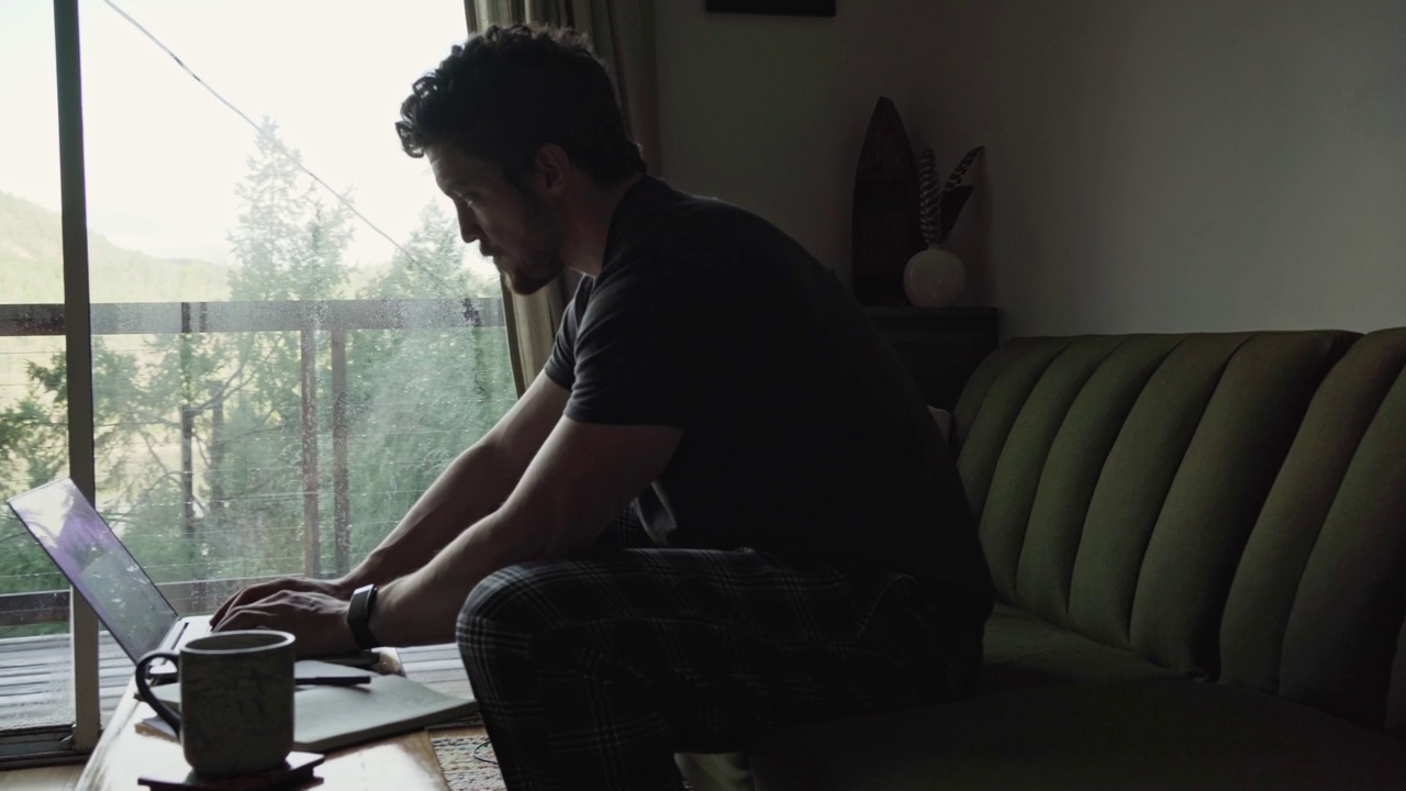 一个穿着睡衣的男人坐在沙发上用笔记本电脑工作视频素材