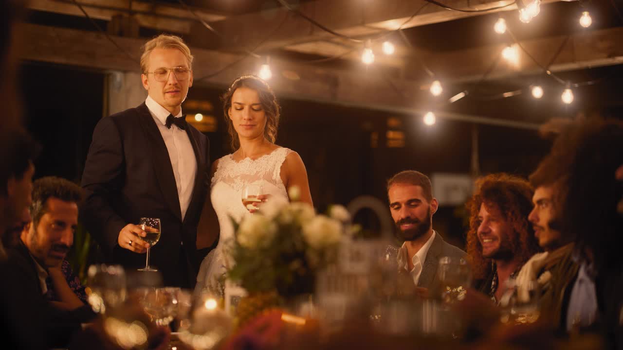 美丽的新娘和新郎在晚会上庆祝婚礼。新婚夫妇与最好的多民族、多样化的朋友们站在餐桌上，为幸福的婚姻敬酒。视频下载