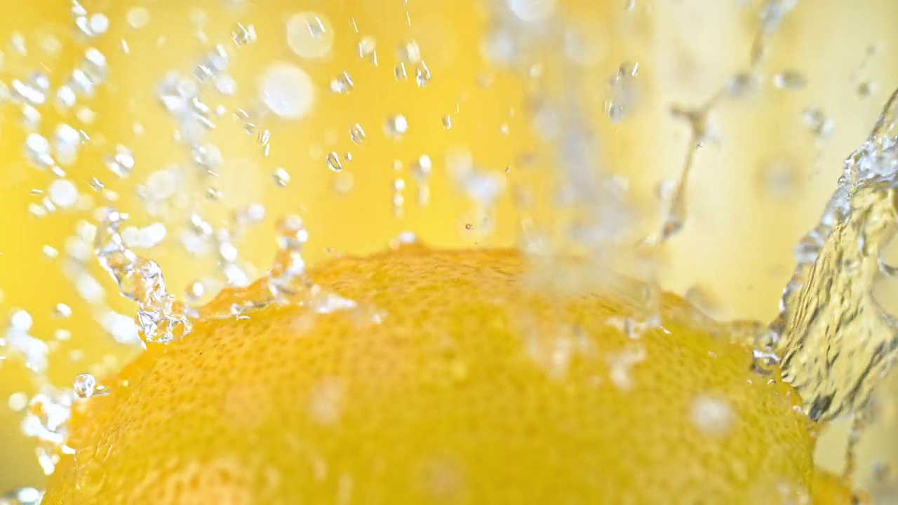 柠檬水果被水泼在黄色背景上的慢动作视频素材