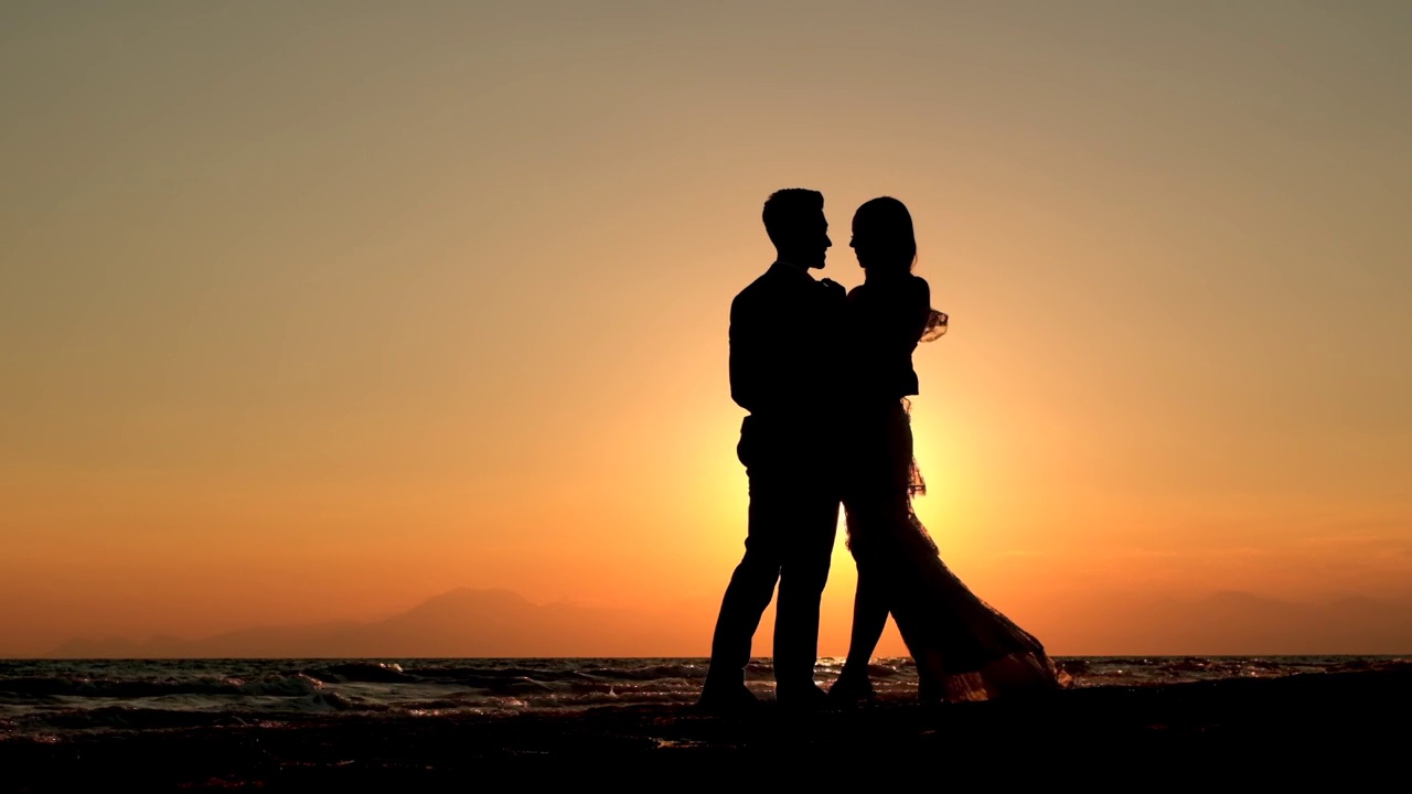 日落时海滩上一对浪漫情侣的剪影视频素材