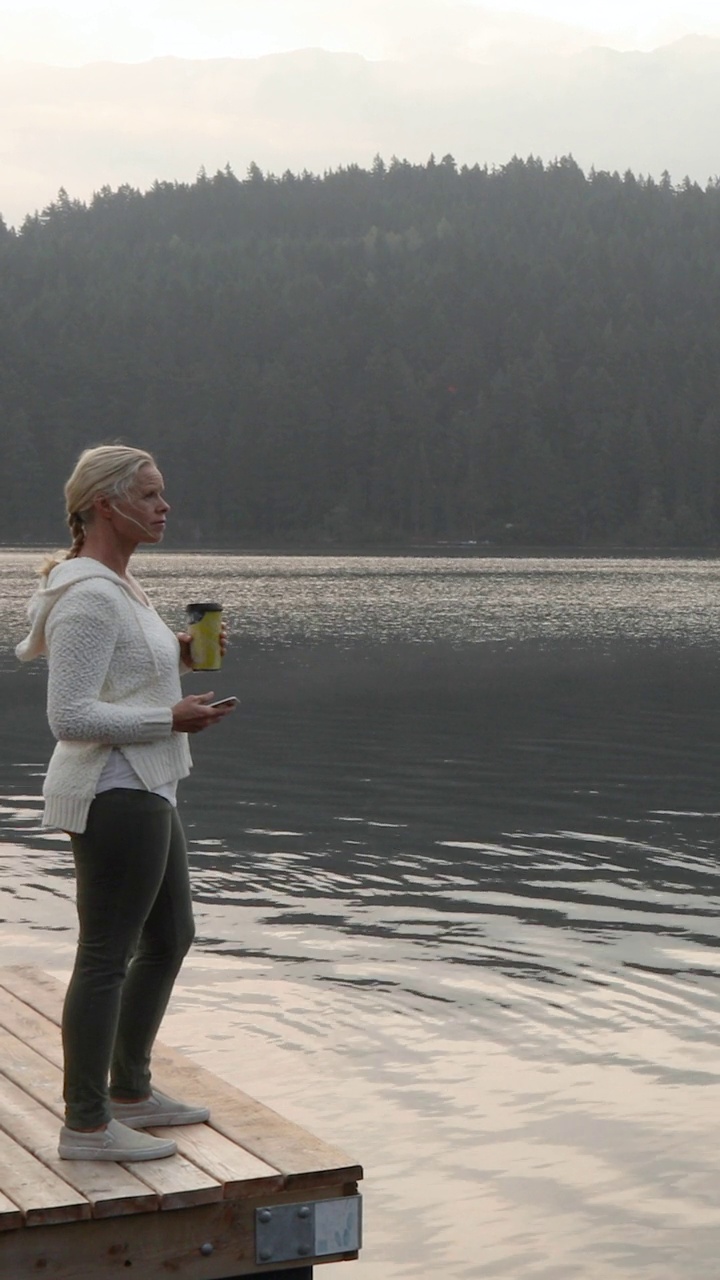 一个女人拿着饮料站在湖边的码头上视频下载